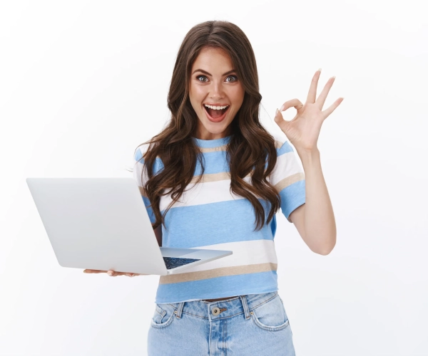 astonished-pretty-caucasian-woman-hold-laptop-look-camera-satisfied-give-approval-show-okay-ok-sign-pleased-rate-good-application-leave-positive-feedback-good-book-review-white-wall